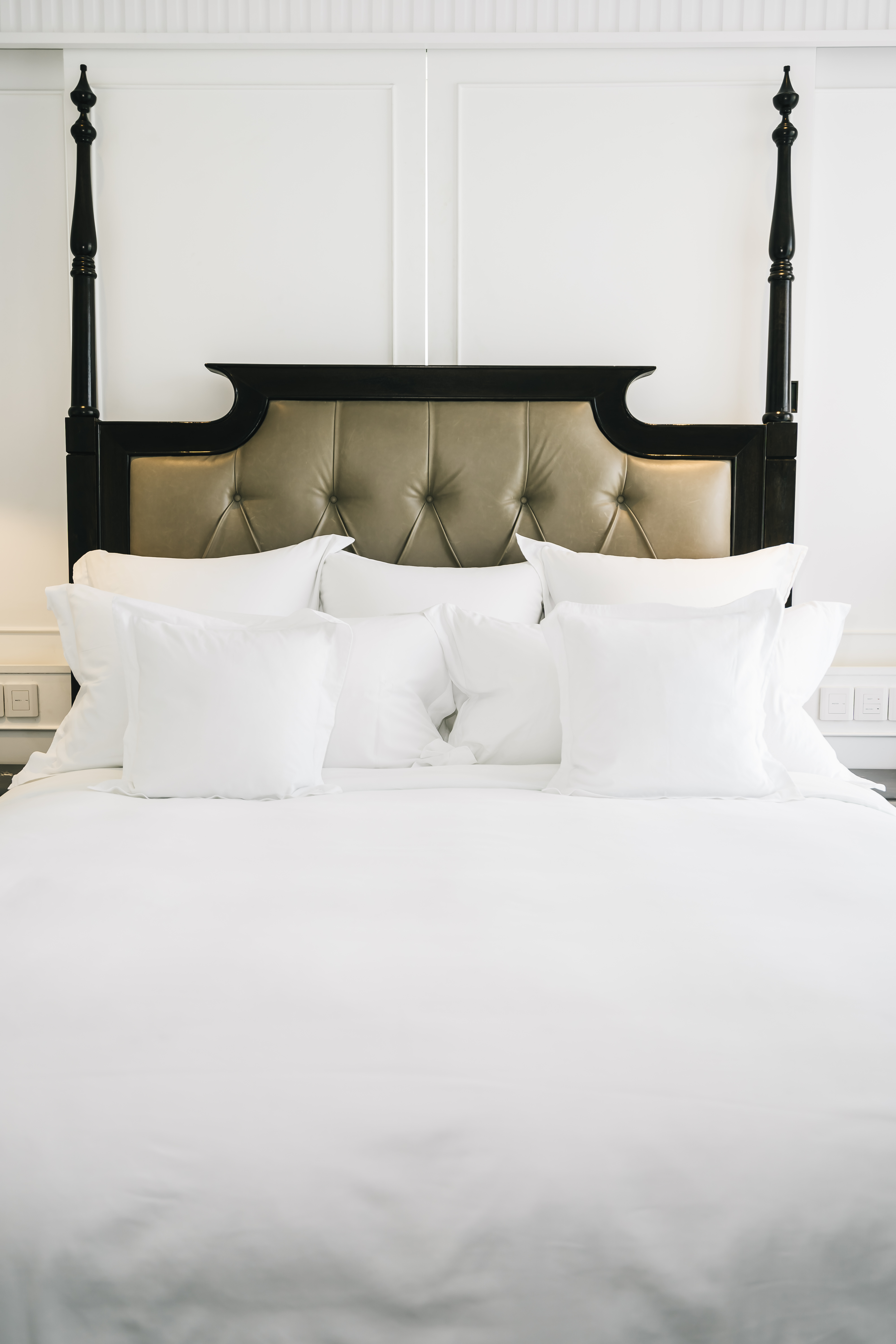 Neatly made bed with white pillows and duvet, featuring a tall dark wooden headboard with leather upholstery.