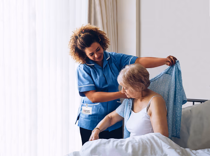 Image of a caregiver assisting a patient with putting a cardigan on.