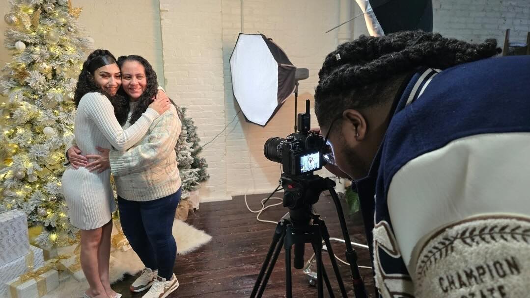 Photographer captures two women hugging near decorated Christmas tree in a cozy indoor studio.