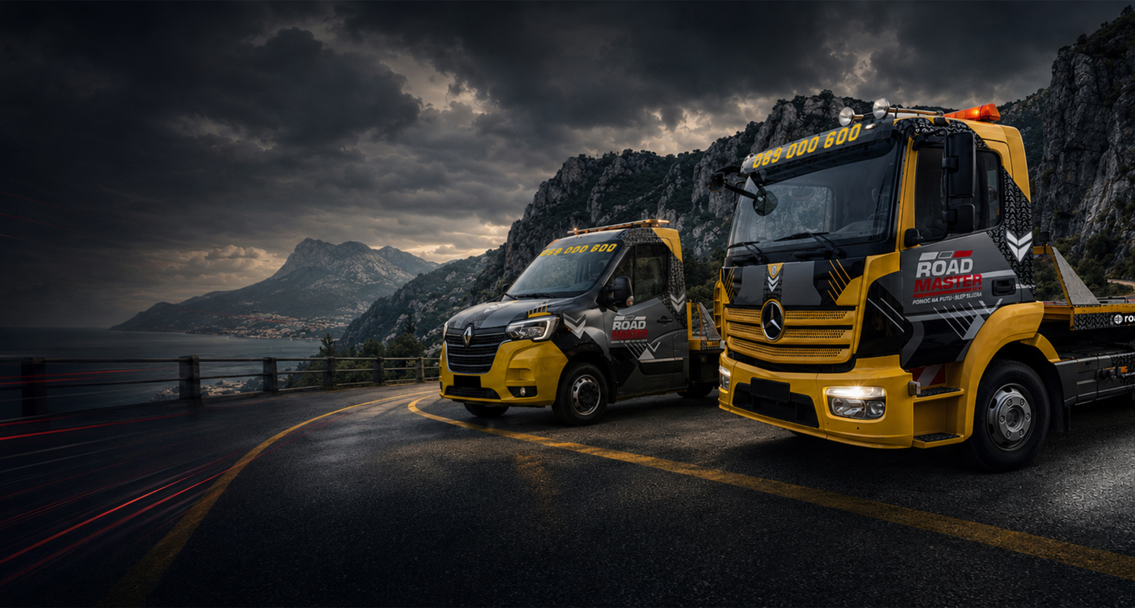 Two yellow and black Road Master tow trucks parked on a curved road with mountains and dark clouds behind.