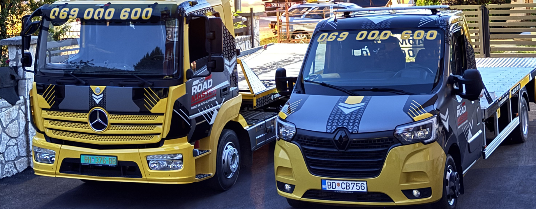 Two yellow and black flatbed tow trucks parked side by side with Road Master branding on the doors.