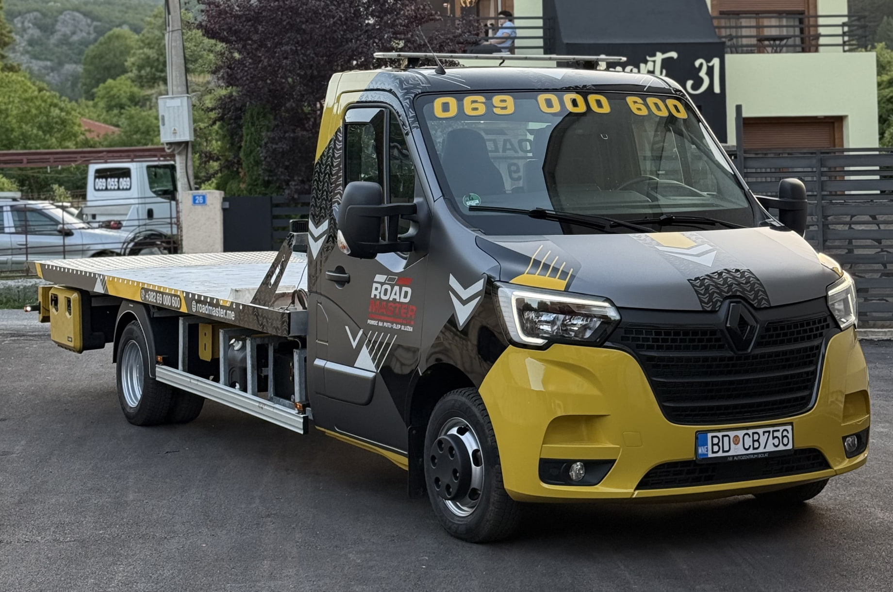 Yellow and black flatbed tow truck with Road Master branding and phone number on windshield and side.