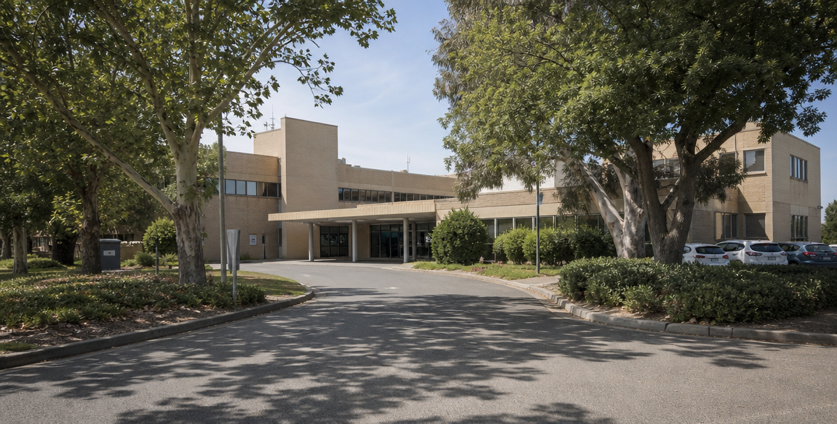 A regional hospital or campus building with a tree-lined approach, reflecting the healthcare and education anchors that sustain population growth.