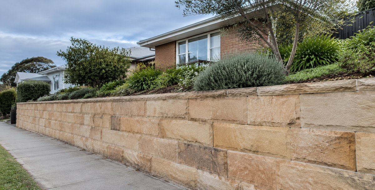 A sandstone retaining wall holding an established Australian garden and home above it, reflecting surplus as what remains once the business is protected.