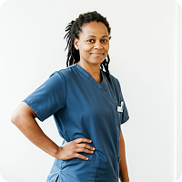 Smiling female healthcare worker with dreadlocks in blue scrubs standing with hand on hip.
