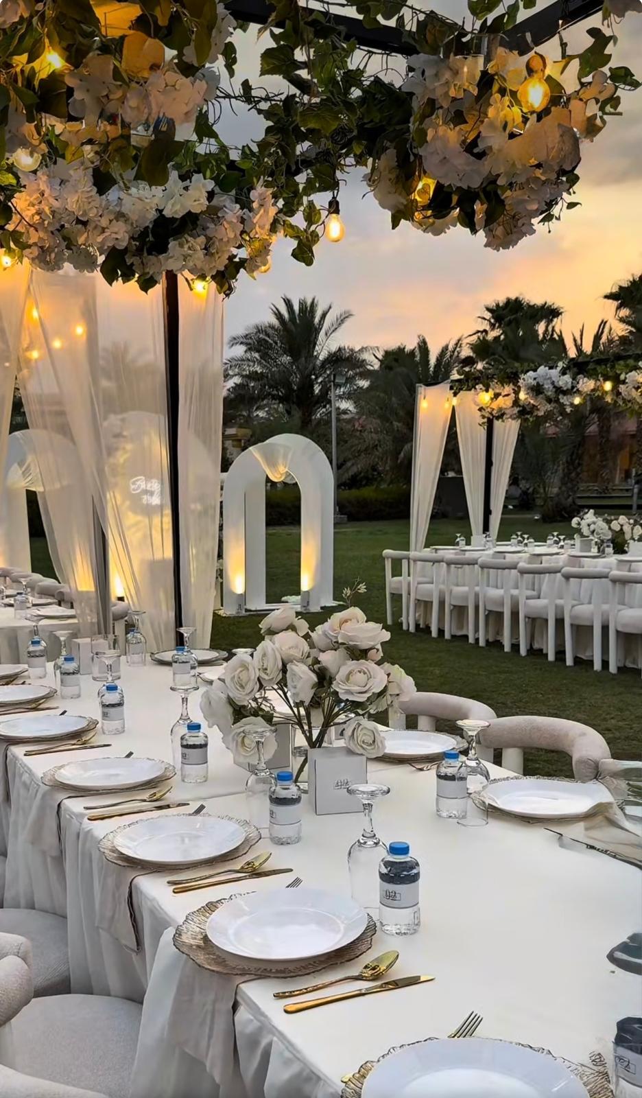 Garden wedding reception with a long dressed table and white florals at dusk
