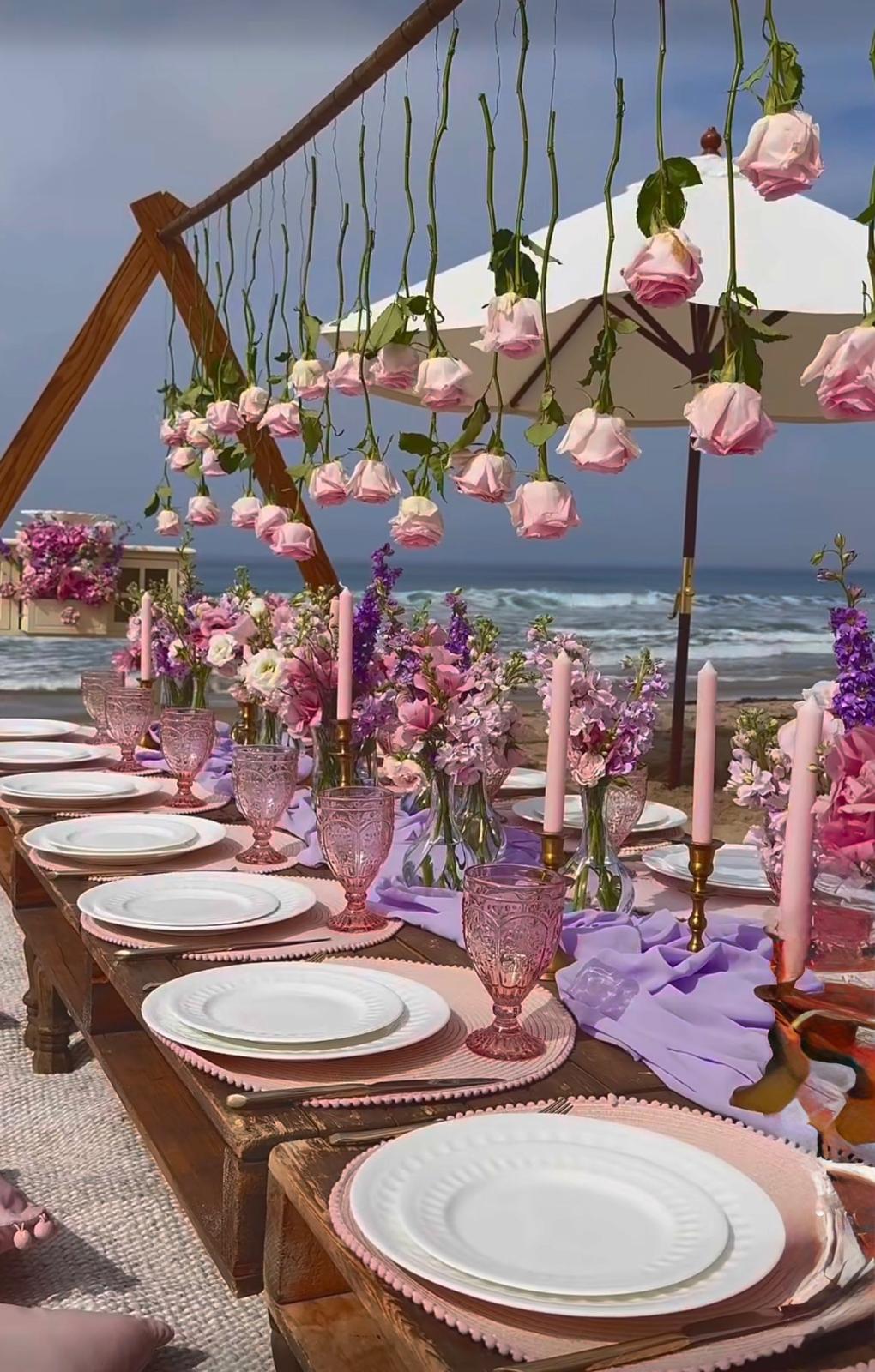 Long table on the beach dressed with pink roses and hanging florals