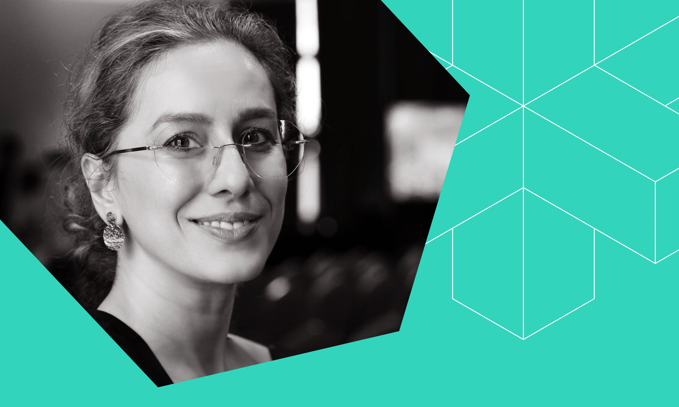 Black and white close-up portrait of a smiling woman with glasses and earrings against a teal geometric background.