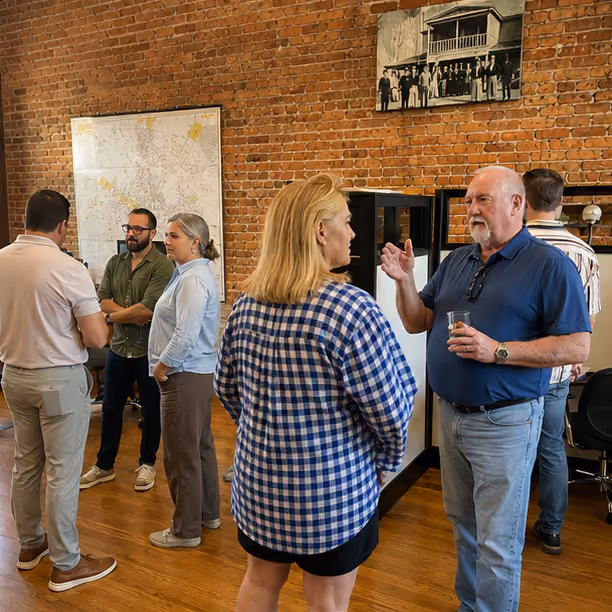 Several people standing and chatting in a room with exposed brick walls and wooden floors.