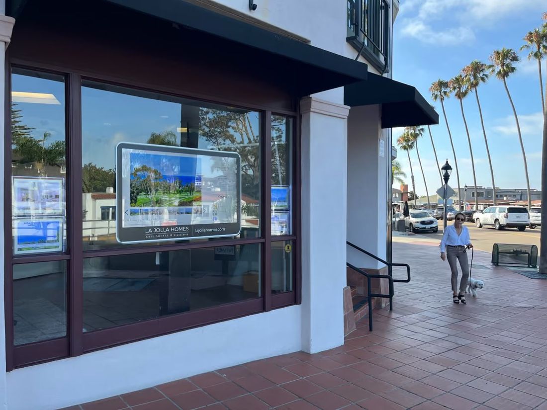 A woman walking her dog past a real estate office window with a WindoVision display