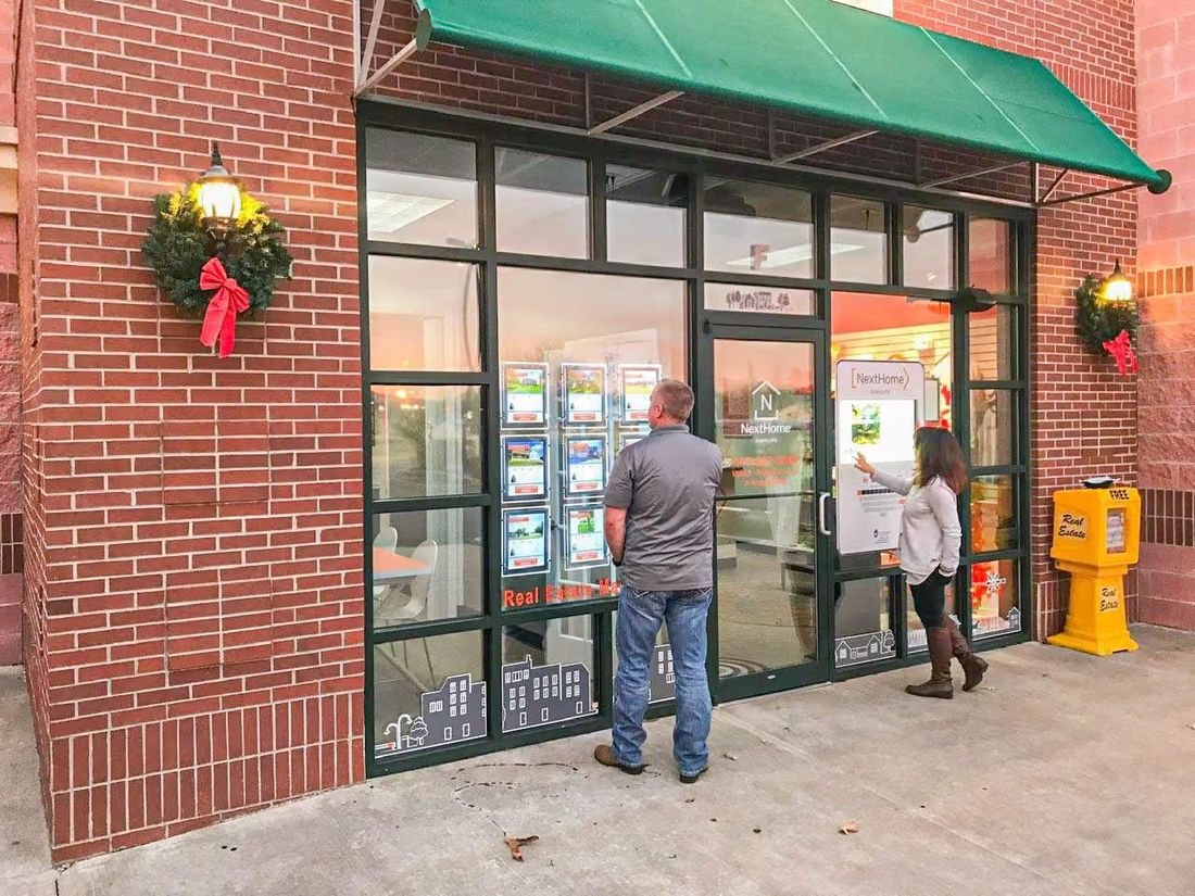 Two people at a real estate office window at dusk, one browsing the display