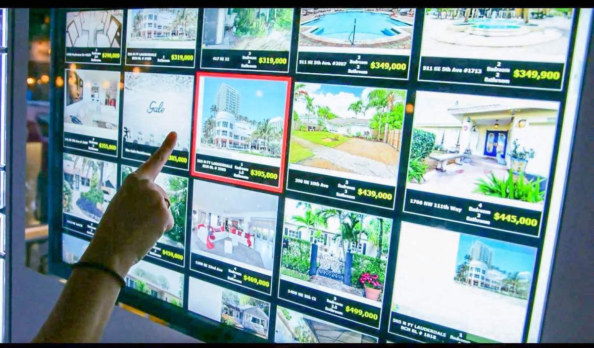 A hand browsing a grid of listings on a WindoVision display