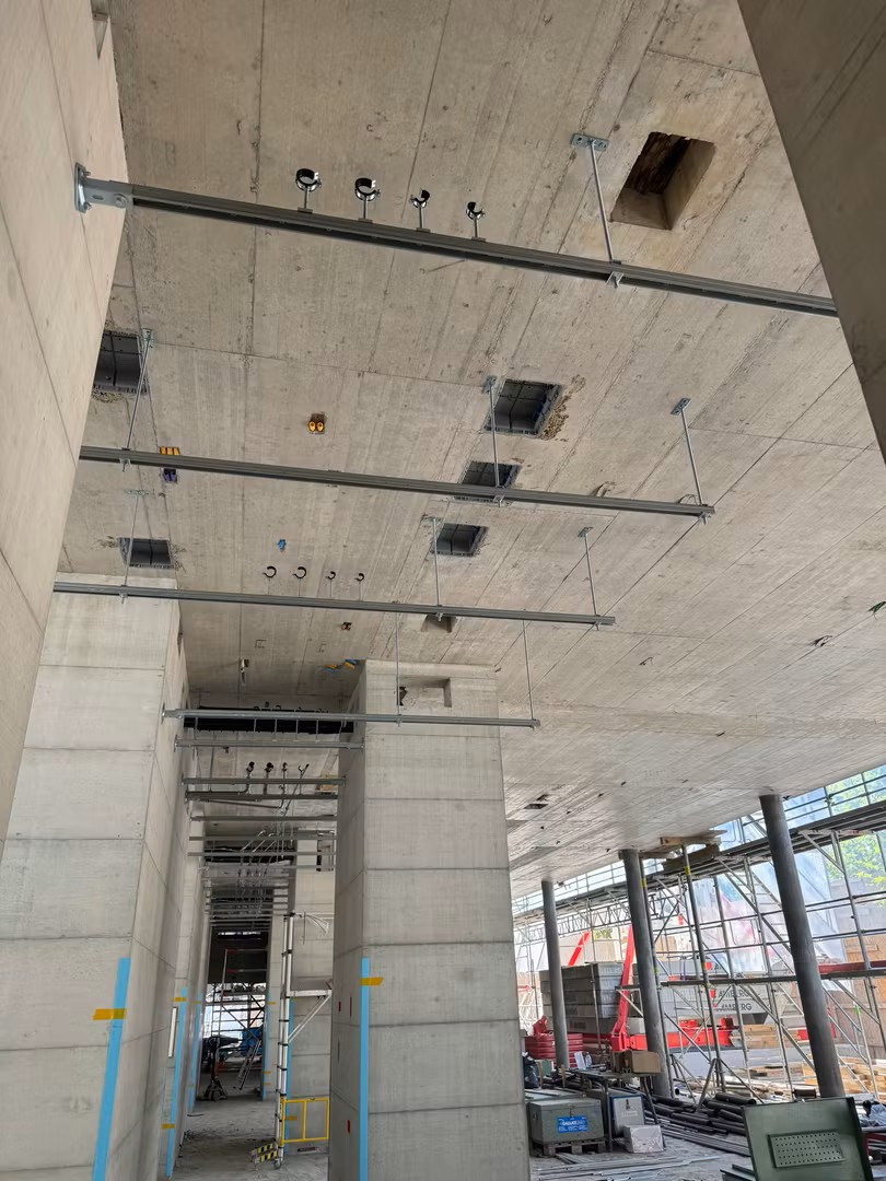Mittlerweile wird an vielen Stellen gleichzeitig gearbeitet: Im 5. Obergeschoss stehen die nächsten Wände und Decken auf dem Programm und auch die Betonelementtreppen bis zur Attika sind bereits auf der Baustelle angekommen.
Während draussen die Unterkonstruktion der Fassade montiert wird, geht es auch im Inneren fleissig weiter. Lüftung, Sanitär und Elektroinstallationen werden nach und nach eingebaut und das Hotel erhält immer mehr von seinem technischen Innenleben. Auch im Untergeschoss geht es weiter: Hier laufen die Randabdichtungen zwischen Boden und Wänden.
Kurz gesagt: Es wird geschalt, montiert, verlegt und abgedichtet – und aus dem Rohbau wird immer mehr ein richtiges Hotel.
