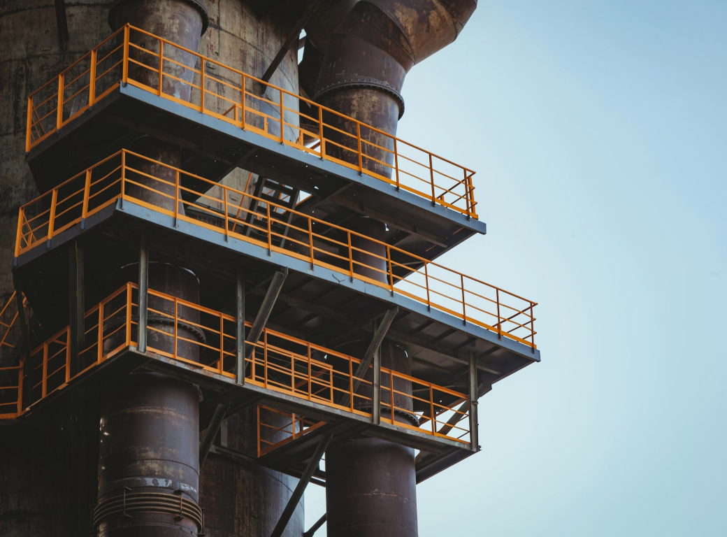 Rusty industrial structure with multiple orange-railed metal platforms against a clear sky.