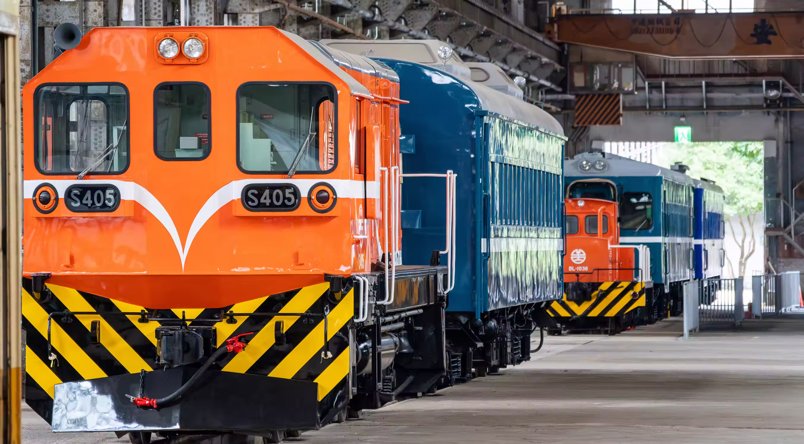 Two orange and blue trains parked on parallel tracks inside a large industrial building.