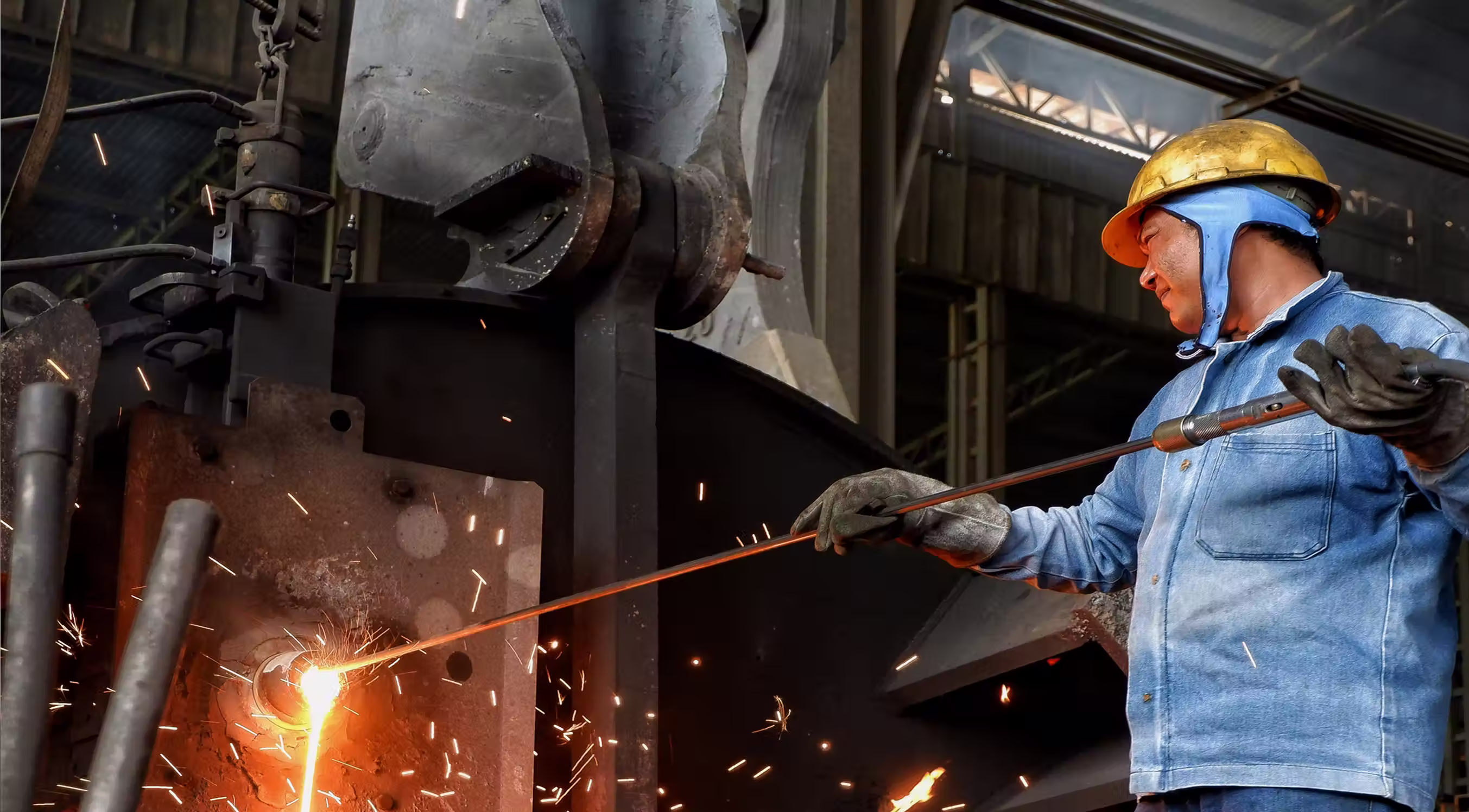 Industrial worker in protective gear pouring molten metal in a foundry with sparks flying.