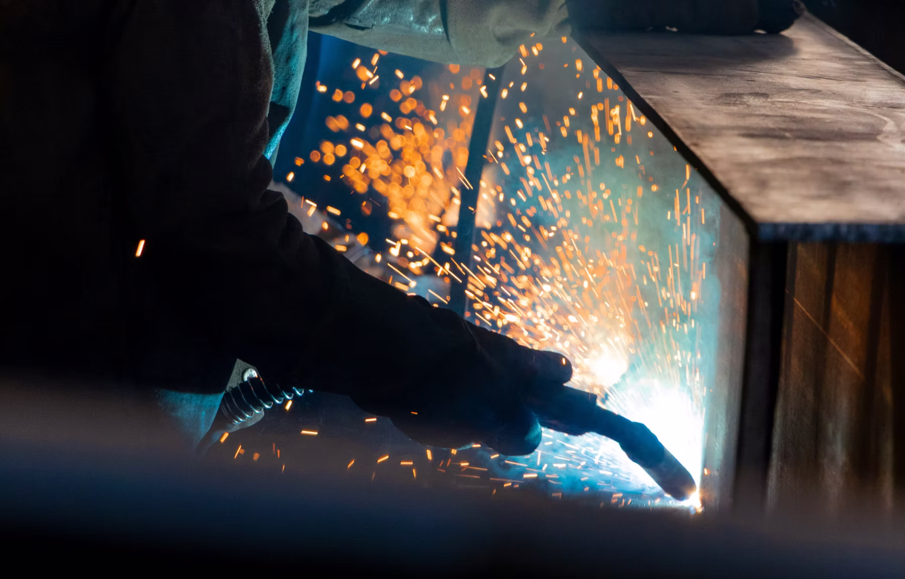 Close-up of a welder's gloved hand working on metal with bright sparks flying around.