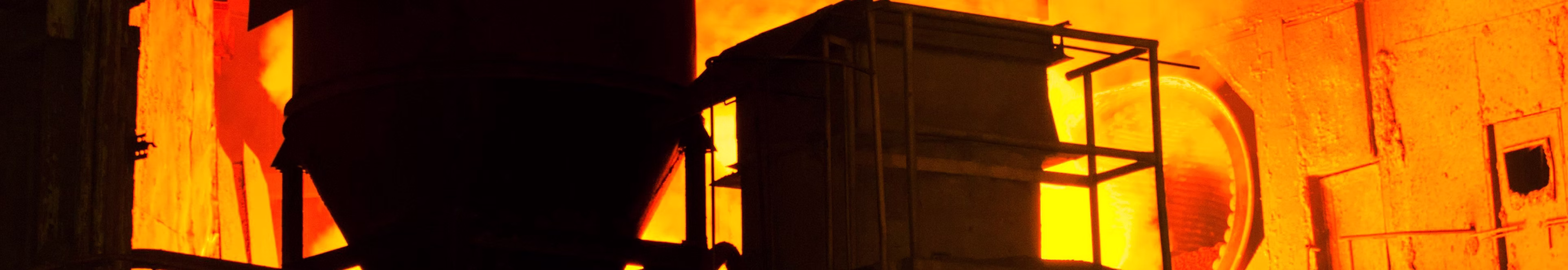 Bright orange furnace fire glowing inside industrial metal structures in a factory setting.