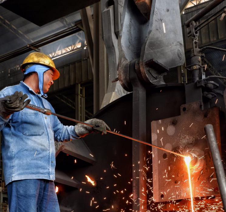 Worker wearing a yellow helmet and gloves operating a metal cutting torch with sparks flying.