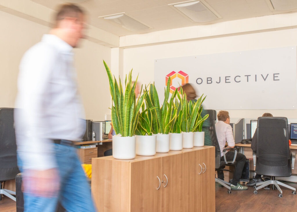an office room with a blurred man in the foreground with the objective logo in focus behind