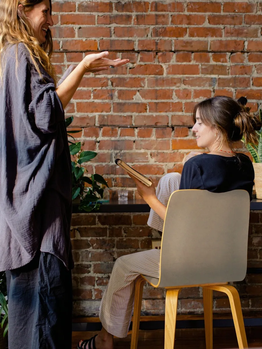 A blonde woman talking to a brunette woman who is sitting down.
