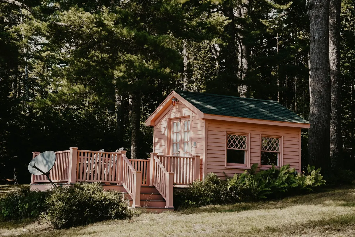 A salmon pink cottage in the woods on a sunny day.