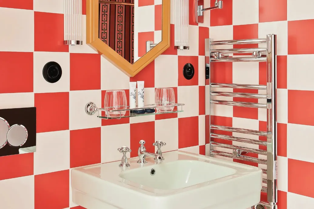 Coin toilette au carrelage en damier corail et blanc avec lavabo à robinetterie chromée, miroir hexagonal à cadre doré, appliques en verre et porte-serviettes chauffant