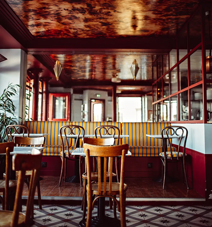 Intérieur de café chaleureux avec une banquette rayée, des chaises en bois, de petites tables et un sol en carrelage à motifs, hôtel Les Deux Gares, 4 étoiles, Paris.
