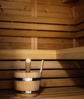 Wooden bucket with a ladle placed on a wooden bench inside a sauna with light wooden walls.