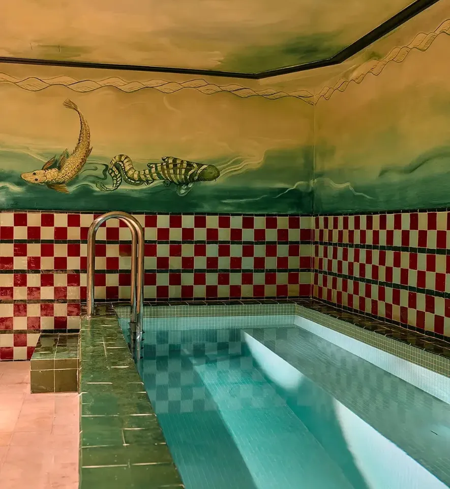 Indoor pool with red and white checkerboard tiled walls, green tile border, and wall paint depicting fish in the water.