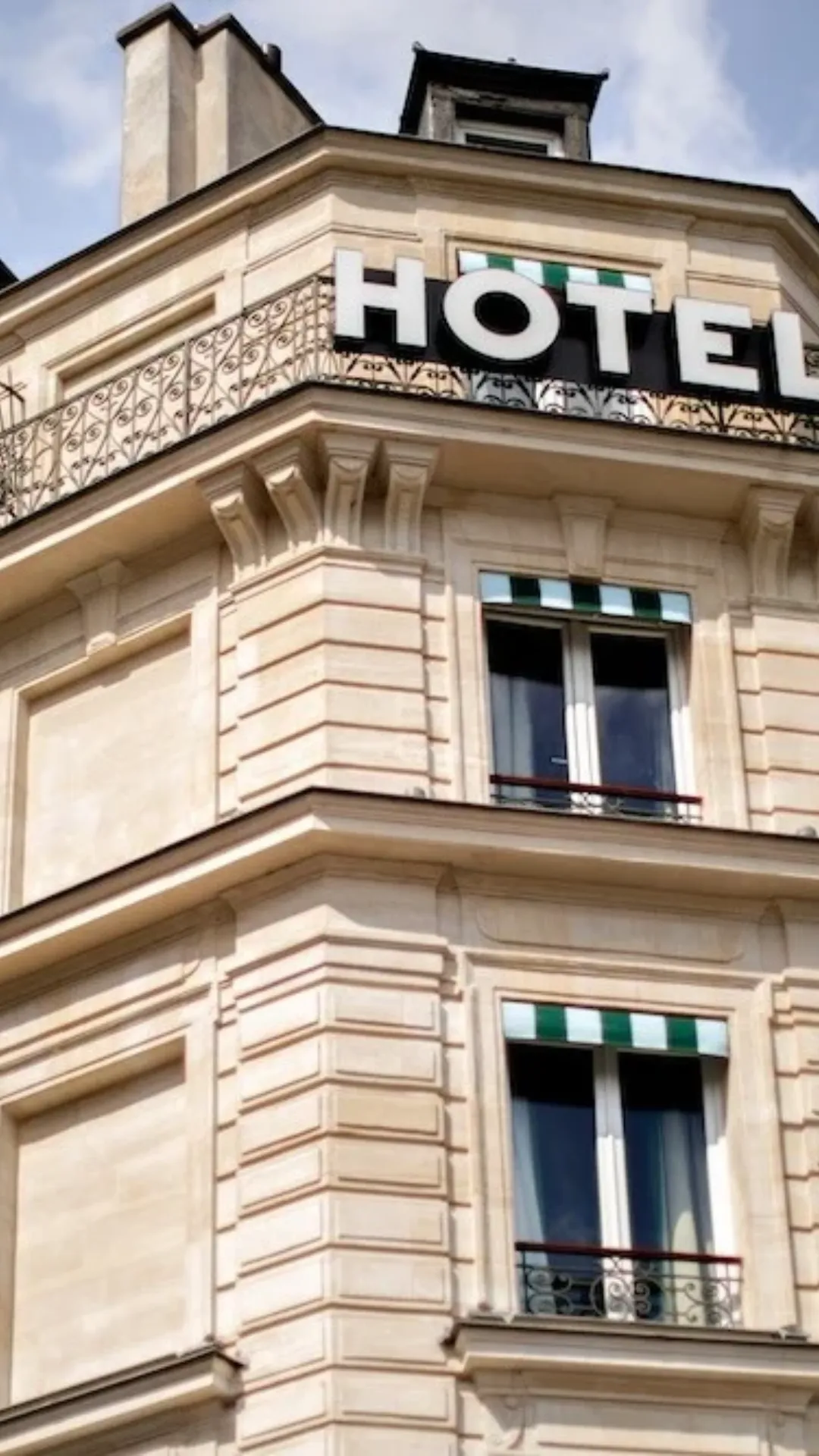 Fenêtres à auvents rayés vert et blanc et balcon en fer forgé, privatisation d’hôtel à Paris 10e