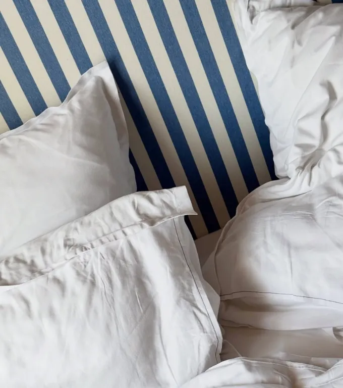 Deux oreillers blancs froissés sur un matelas avec une housse à rayures bleues et blanches.
