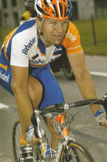 Steven de Jongh in Rabobank team jersey and helmet riding a racing bike on a paved road.