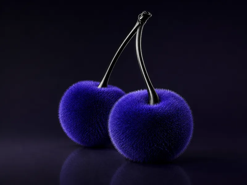 Two fuzzy textured blue cherries with black stems on a reflective dark surface.