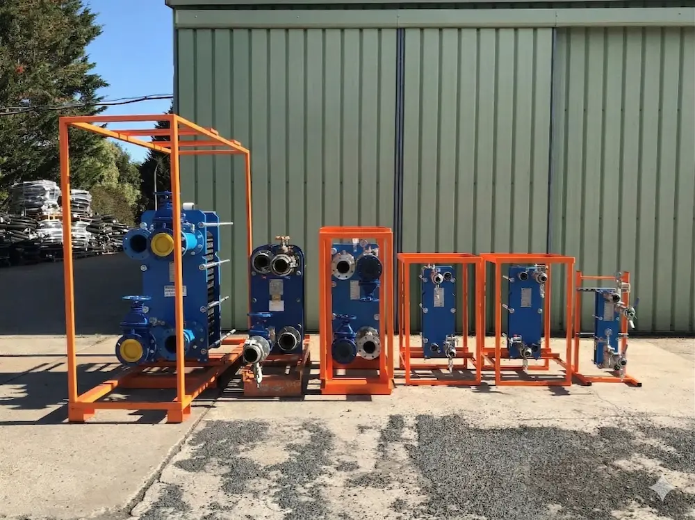 Ensemble de plusieurs échangeurs de chaleur industriels bleus encadrés par des structures métalliques orange, alignés devant un bâtiment en métal vert.