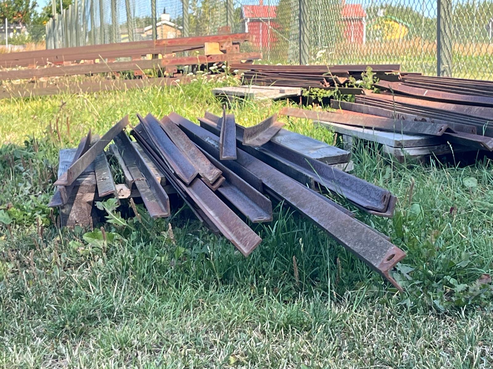 Salvaged steel beams stacked on grass at a demolition site.