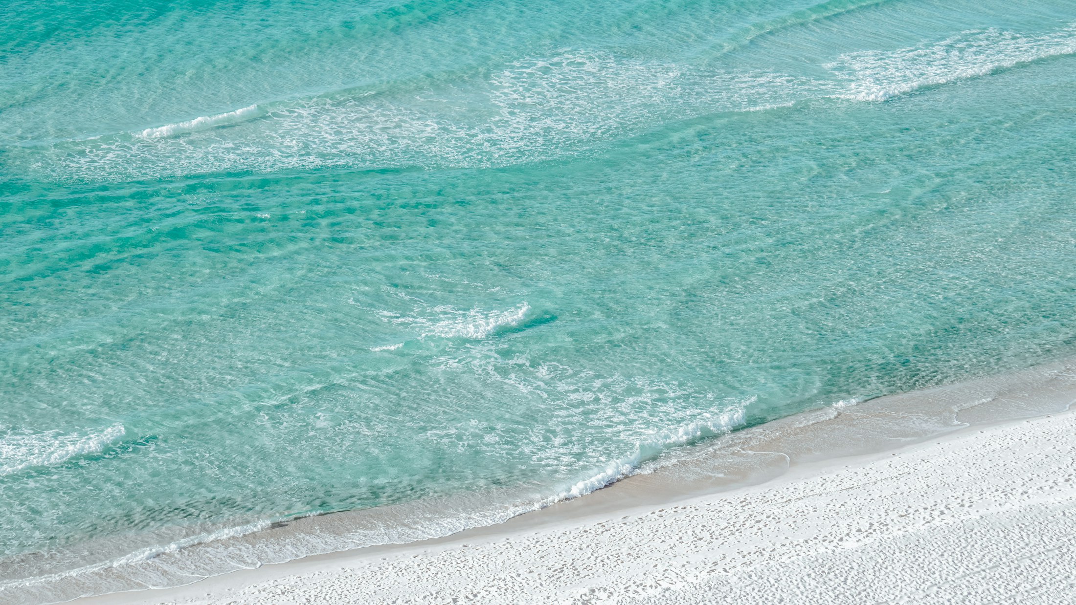 Bright turquoise surf rolling onto white sand, aerial view