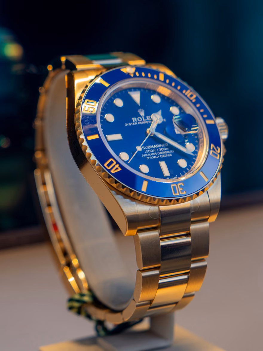 A men's blue and gold luxury watch in warm light, held in trust