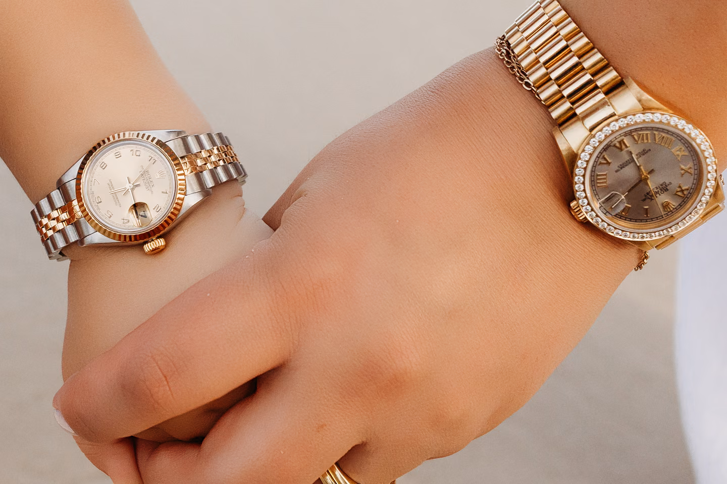 Two luxury watches worn on clasped hands over the sand