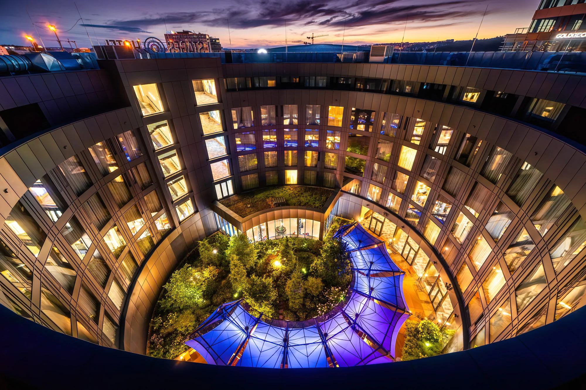 Vnitřní atrium hotelu Stages s nasvícenou skleněnou střechou za soumraku