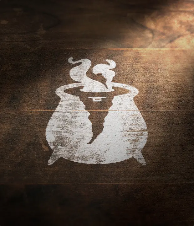 White logo of a steaming witch's cauldron on a wooden surface.