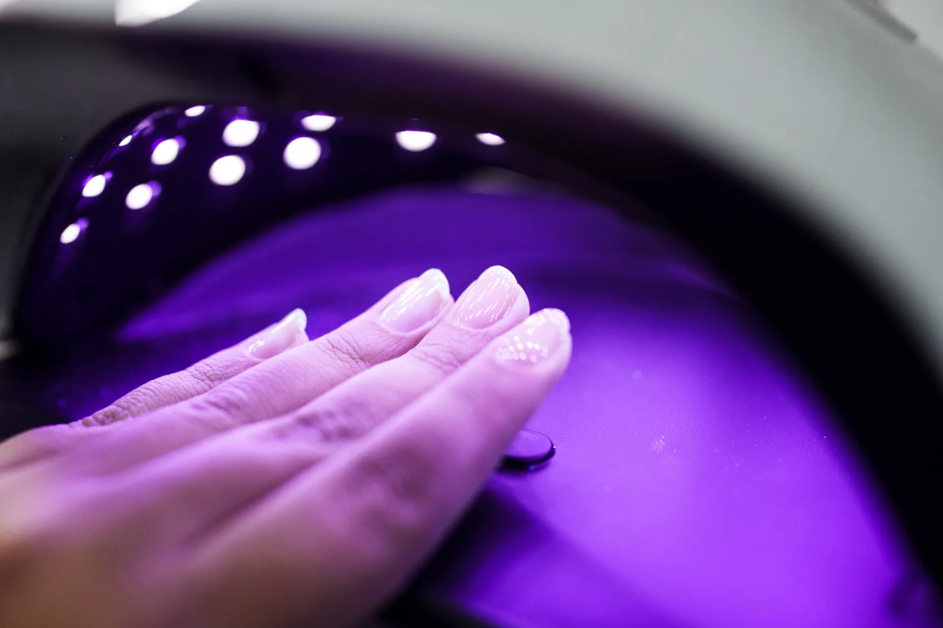 Hand with freshly cured shiny nails under a purple UV light dryer at Compass Career College
