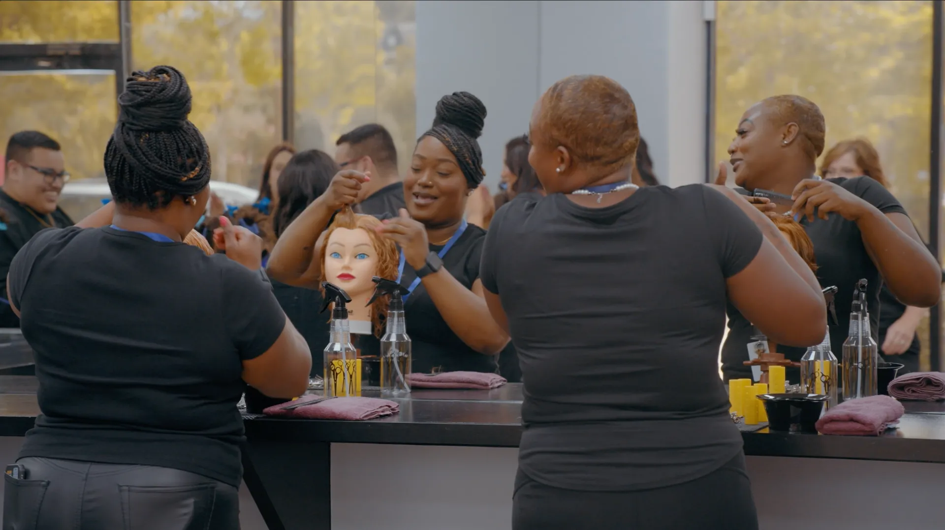 Two Compass Career College hairstylists practice on mannequin heads in a salon with mirrors and tools on the counters.