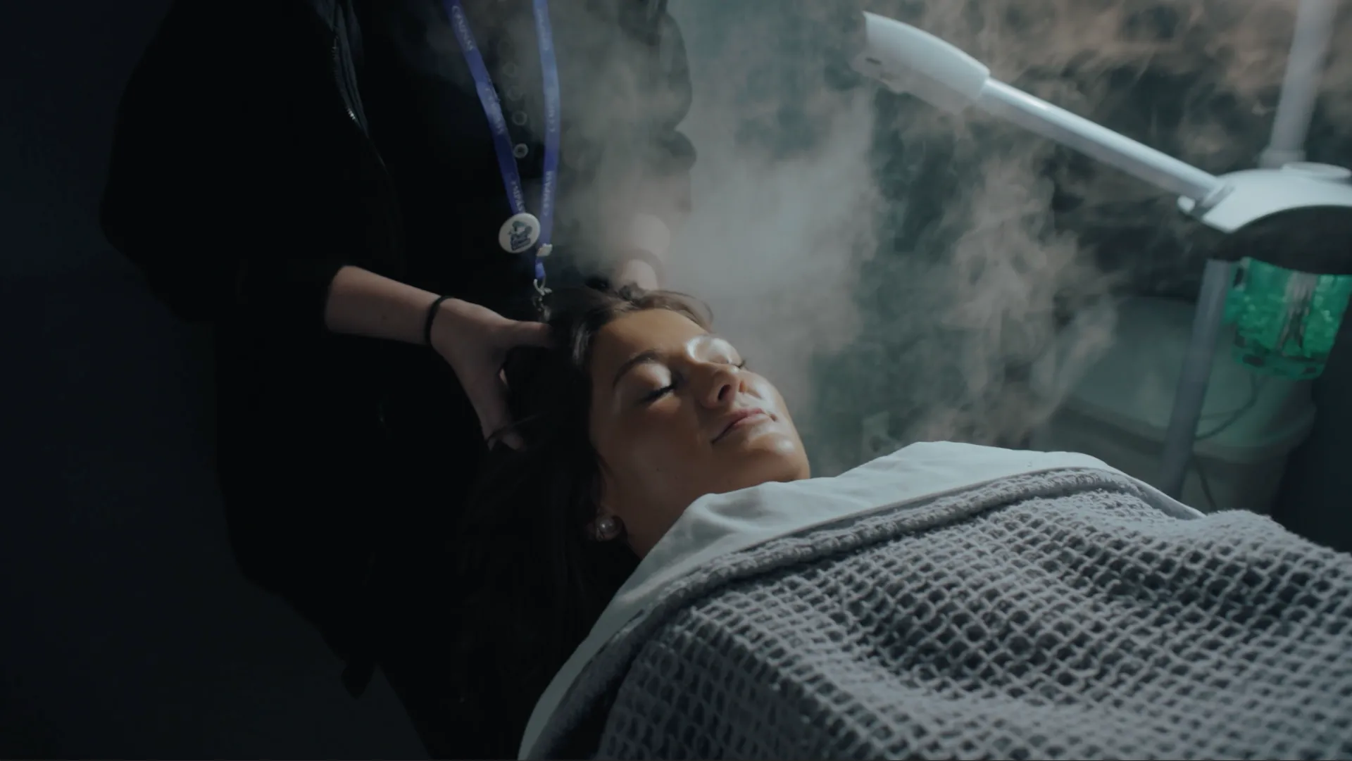 Woman relaxing with eyes closed while receiving a facial steam treatment at a Compass Career College Salon