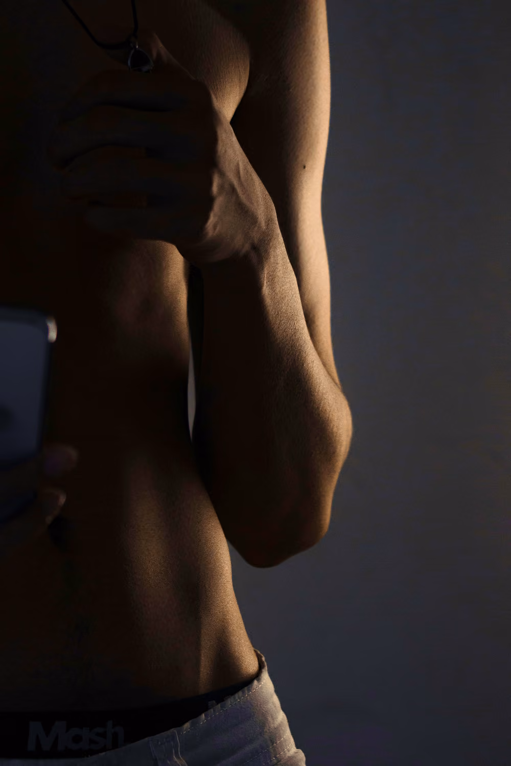Close-up of a person holding their arm, showing muscles and shadows on skin.