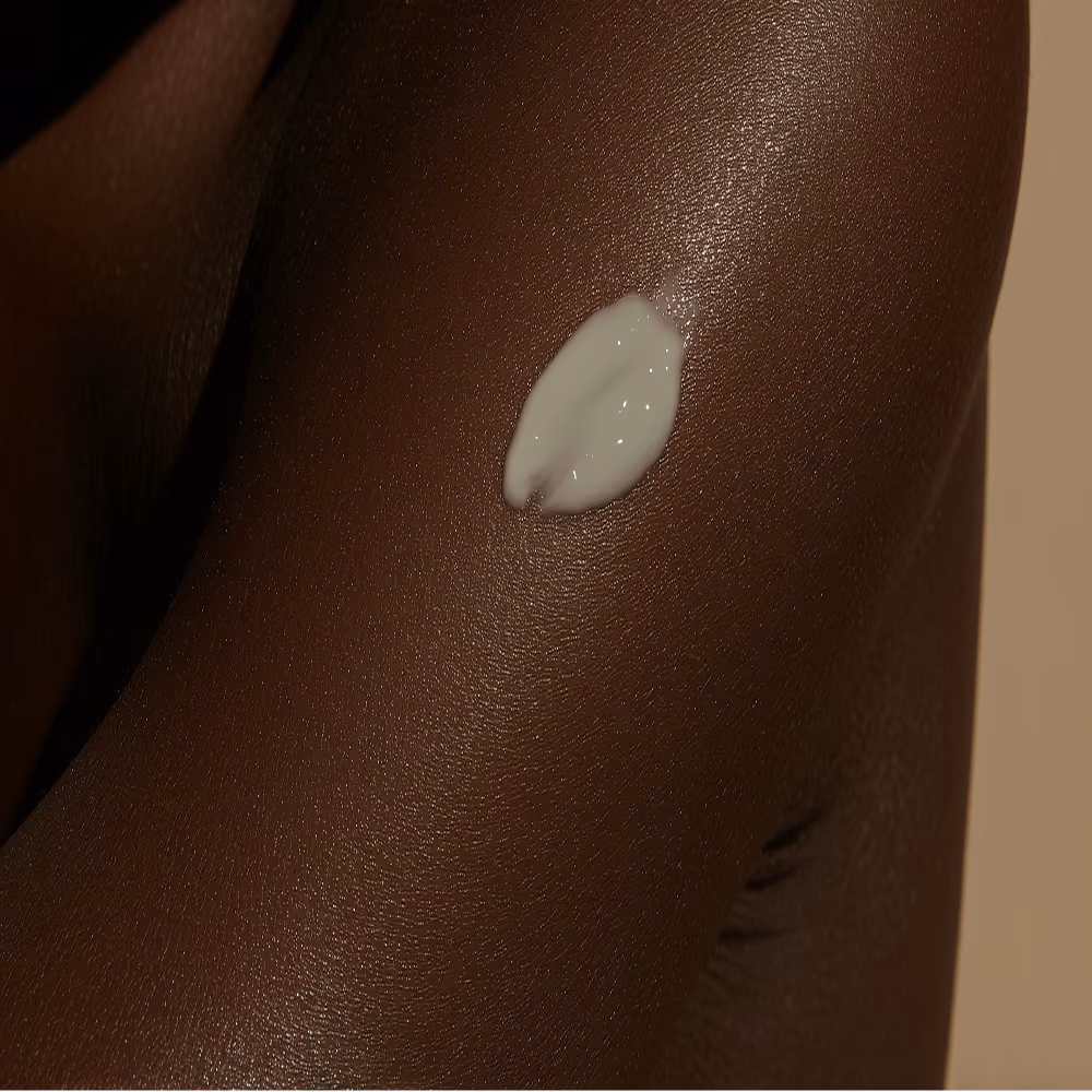 Close-up of dark skin with a small dollop of white cream on the upper arm.
