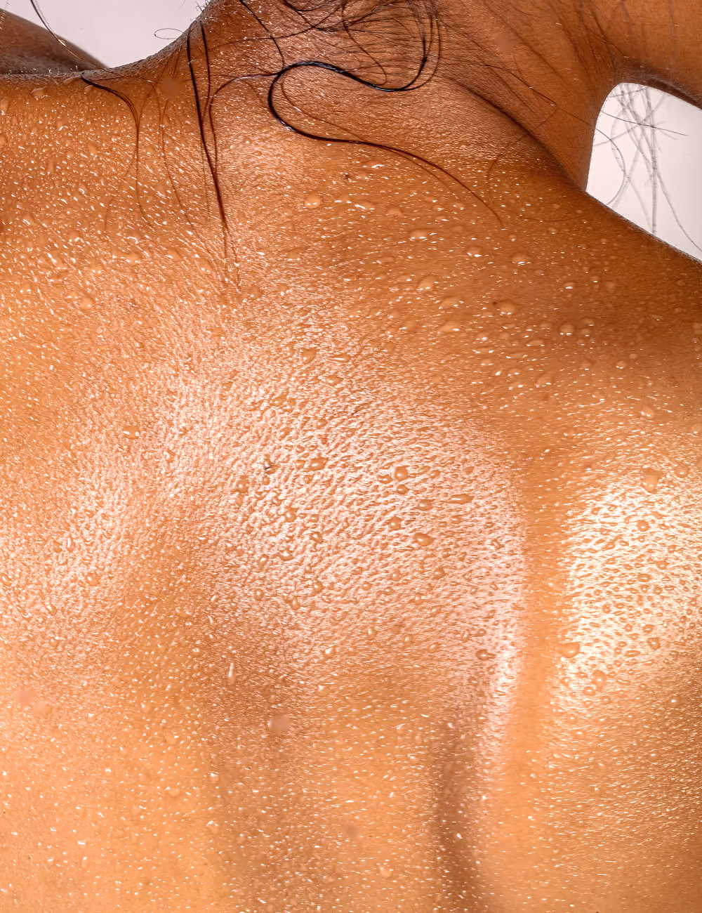 Close-up of a wet and glistening human shoulder and upper back with water droplets.