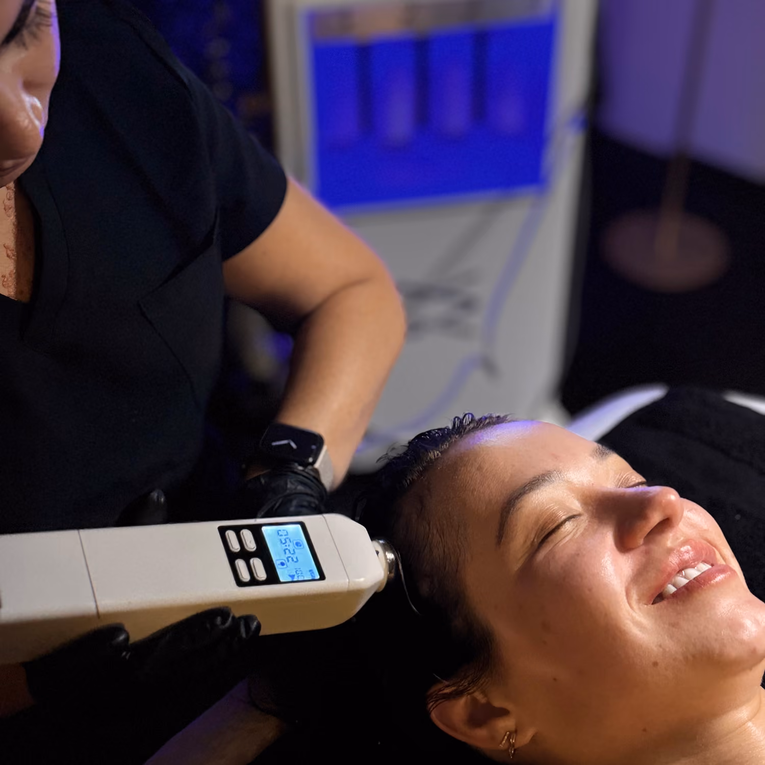 Woman smiling with eyes closed while receiving a scalp treatment with a handheld device.
