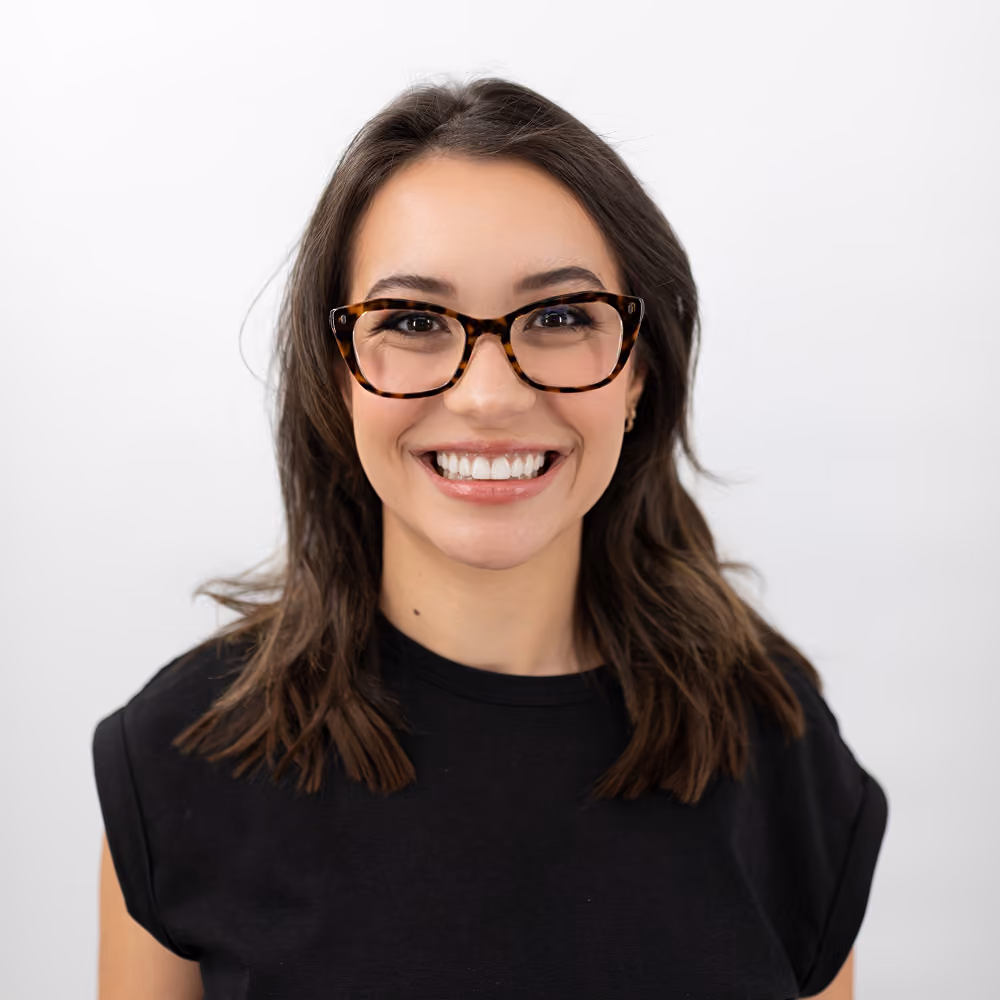 Smiling woman with glasses and shoulder-length brown hair wearing a black shirt on white background.