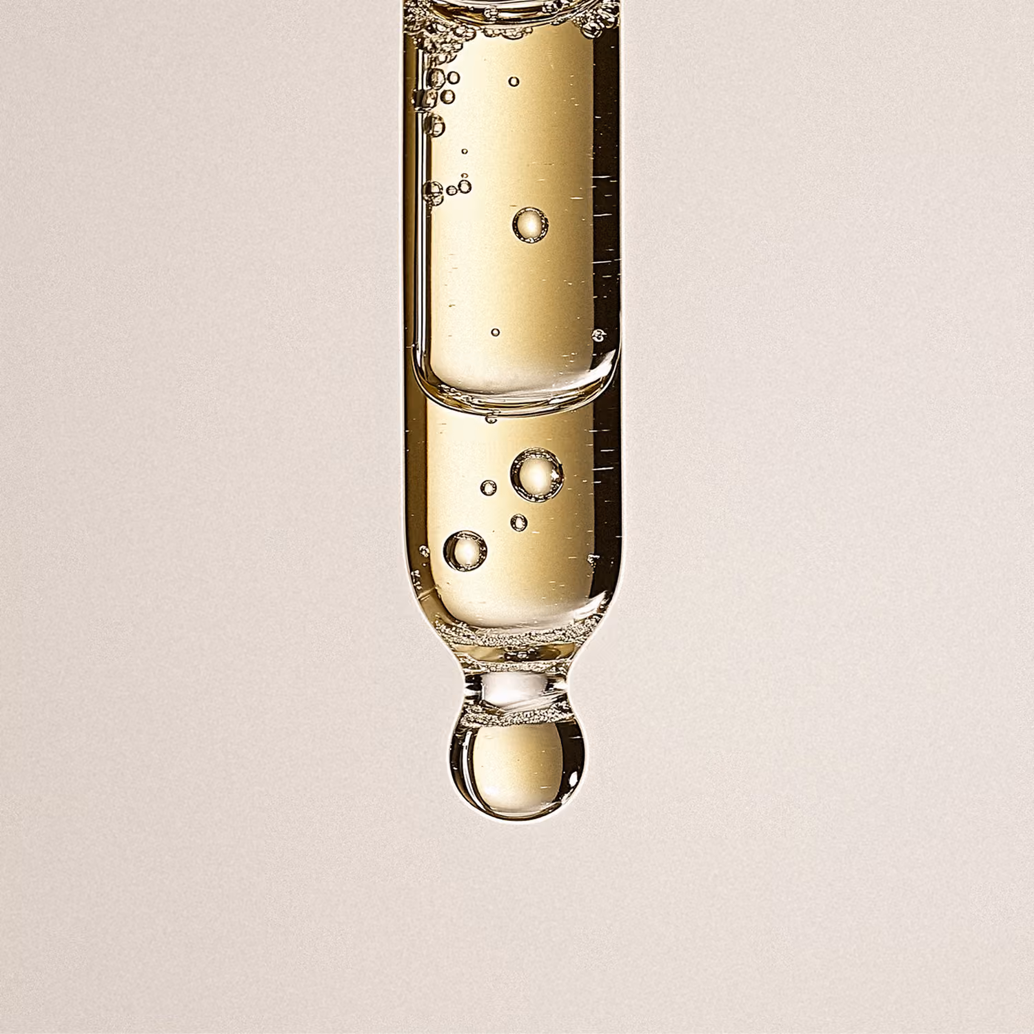 Close-up of a dropper with a golden liquid and air bubbles inside.